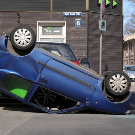 Foto: Auto sadursmē Rīgā spēkrats apgāzies uz jumta