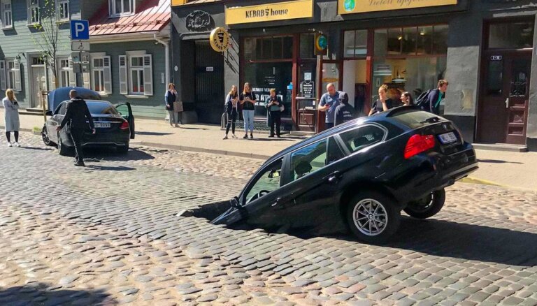 Foto: Ģertrūdes ielas bruģī ielūzis BMW; 'Rīgas siltums' uzņemas atbildību
